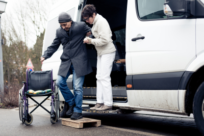 Caregiver woman helping with care to senior man exit a van